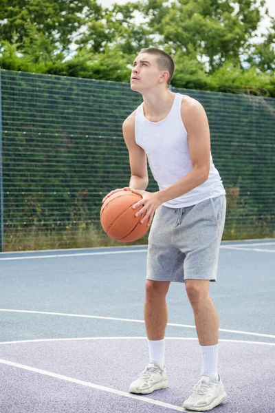 19 yaşında bir ergen çocuk halka açık bir parkta basketbol sahasında şut çekiyor.