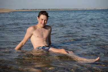 A 17 Year Old Teenage Boy Sitting In The Surf