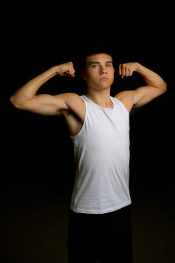 19 yaşında, kollarını kasan kolsuz tişörtlü bir çocuk.