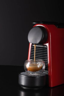 Şık küçük kırmızı kapsül kahve makinesi iki duvarlı güzel bir fincanda sıcak espresso hazırlıyor. Taze demlenmiş kahveye bayılırım. Seçici odak.