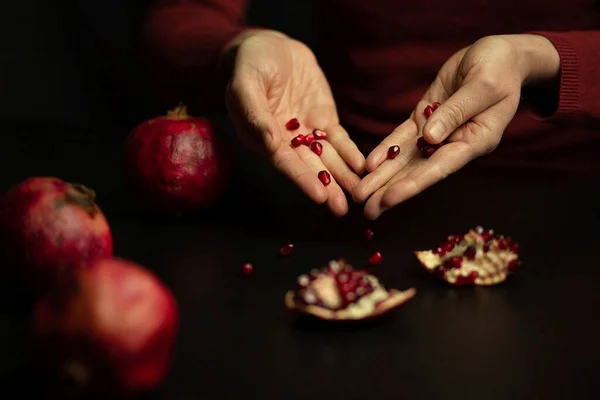 womens elegant white hands and red pomegranate seeds in their hands and on the table symbolize the feminine nature, the other three red ripe pomegranates are also lying on the table nearby High