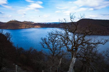 Sonbaharda ya da kışın alçak dağlarla çevrili bir dağın eteğindeki göl Hesse Almanya 'sındaki Edersee' de mavi bir gökyüzünün altında yapraksız ağaçlarla çevrilidir. Yüksek kalite fotoğraf