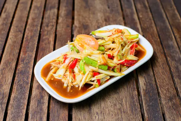 Baharatlı papaya salatası, ahşap arka planda tuzlanmış yengeç ve mayalanmış balık..