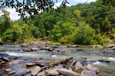 Bu, güneşli bir günde büyük bir dere boyunca uzanan bazı akıntıların ve kayaların uzun bir görüntüsü..