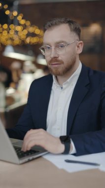 Dikey video. İş adamı çalışırken kameraya zevkle bakar..