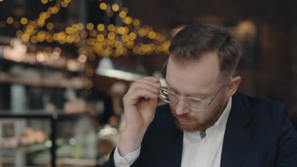 Podnikatel si vytahuje brýle a cítí se unavený v kavárně. — Stock video