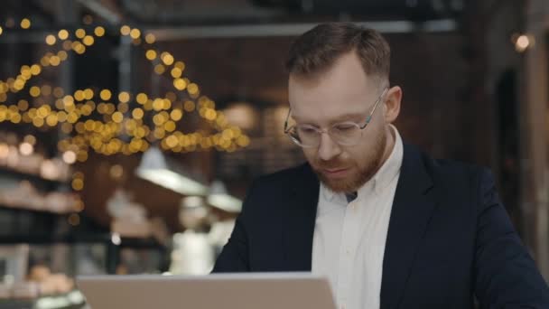 Ο άνθρωπος κάθεται στο τραπέζι και εργάζεται σε φορητό υπολογιστή στο καφέ. Σύμβαση ανάγνωσης επιχειρηματιών. — Αρχείο Βίντεο