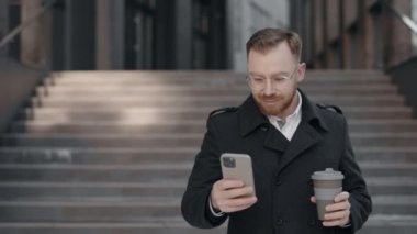 İş adamı akıllı telefondan mesaj atıyor ve elinde bir fincan kahve tutuyor..