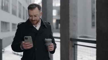 İş adamı akıllı telefondan mesaj yolluyor ve elinde bir fincan kahve tutuyor..