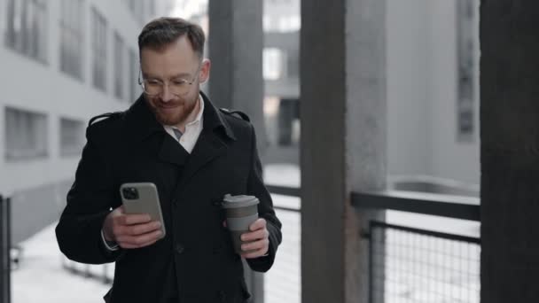 Geschäftsmann schreibt SMS auf Smartphone und hält Tasse Kaffee to-go. — Stockvideo
