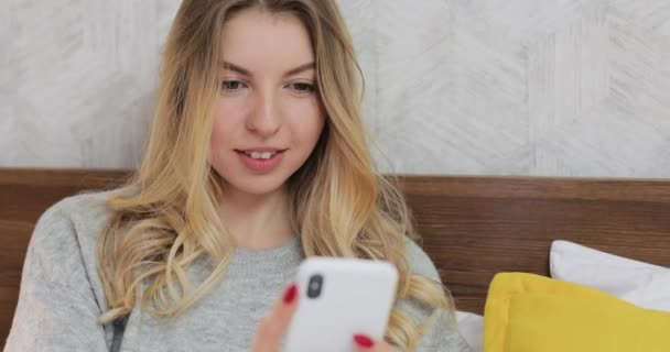 Kaukasische Frau liegt auf ihrem Bett, blättert herum und chattet auf dem Smartphone. — Stockvideo