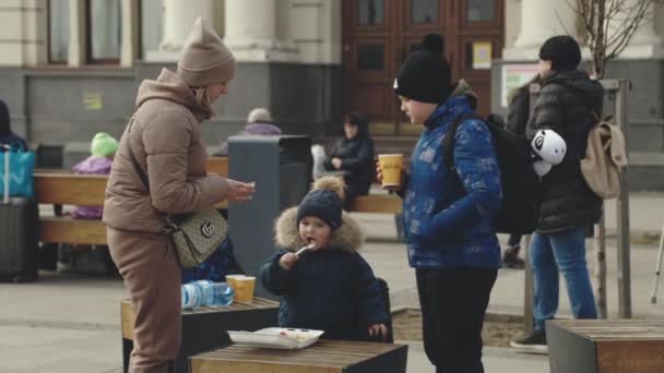 Львов, Украина - 15 марта 2022 года: Жители железнодорожного вокзала западноукраинского города Львов ждут эвакуационных поездов. Дети едят рядом с матерью или волонтером. Концепция войны на Украине. — стоковое видео
