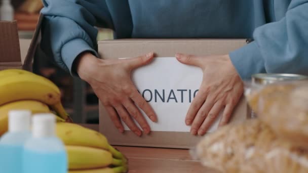 Крупный план женщины, приклеивающей бумагу со словом пожертвование на коробке — стоковое видео