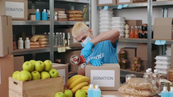 Человек в маске упаковывает коробку с едой для пожертвований — стоковое видео