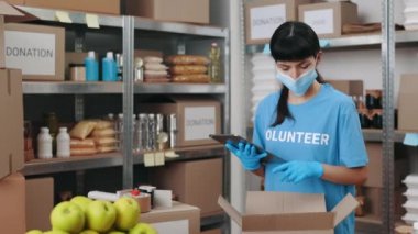 Maskeli ve eldivenli kadın yardım deposunda tablet kullanıyor.