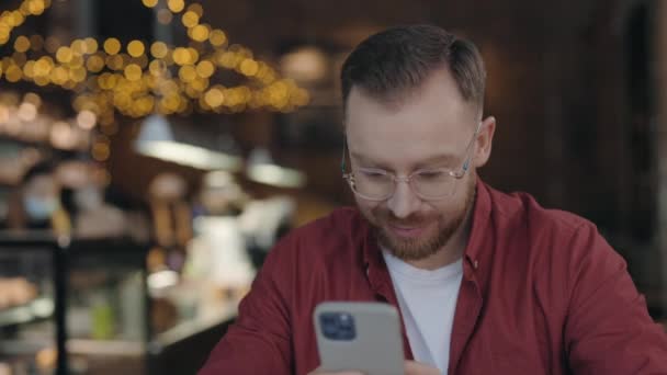 Mann programmiert Nachrichten auf dem Smartphone, während er im Café arbeitet. — Stockvideo