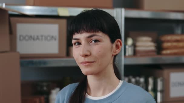Volontaire féminine posant à la banque alimentaire avec des étagères pleines — Video