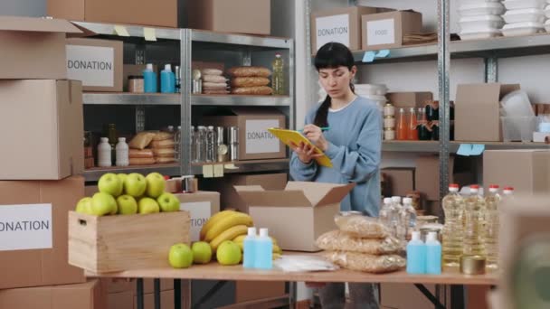 Femme écrivant sur presse-papiers parmi les entrepôts de banque alimentaire — Video