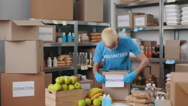Mann mit Mundschutz bereitet Spendenbox in Lagerhalle vor — Stockvideo