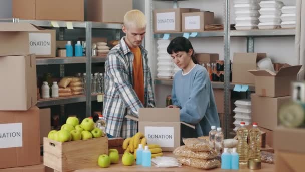 Jovem e mulher embalando alimentos para doação — Vídeo de Stock