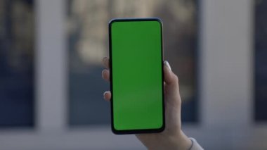 İş kadını caddede dikey olarak yeşil ekranlı telefonu tutuyor ve ona dokunuyor.