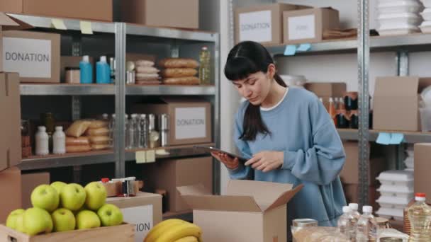 Femme utilisant tablette numérique lors de l'emballage boîte pour le don — Video