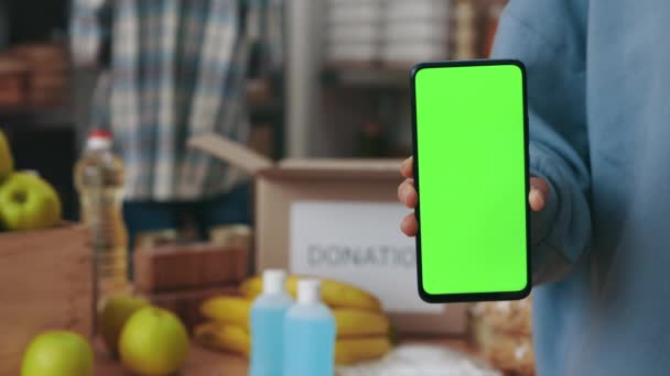 Vrouw met groene smartphone op het scherm bij de voedselbank — Stockvideo