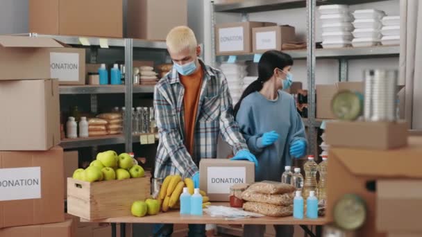 Trabajadores de la caridad en máscaras faciales preparando cajas con comestibles — Vídeos de Stock