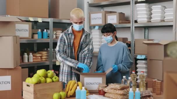 Trabajadores sociales en máscaras faciales empacando comida en cajas — Vídeos de Stock