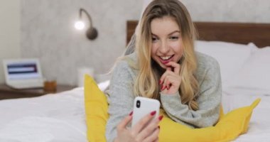 Akıllı telefon kamerasından selam veren ve yatak odasında konuşmaktan zevk alan bir kadın..