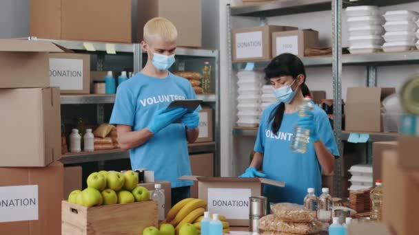 Tým dobrovolníků v obličejových maskách pomocí tabletu v potravinové bance — Stock video