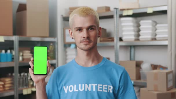 Junger Mann hält Handy mit grünem Bildschirm bei Lebensmittelbank — Stockvideo