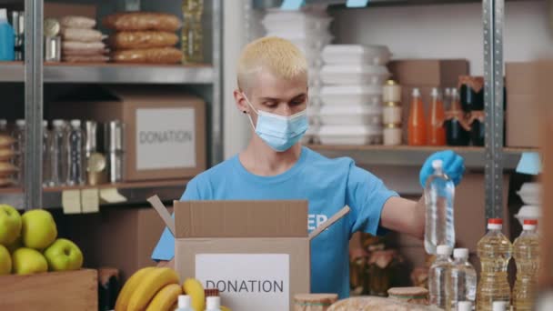 Мужчина упаковывает коробки для пожертвований в маску и перчатки — стоковое видео