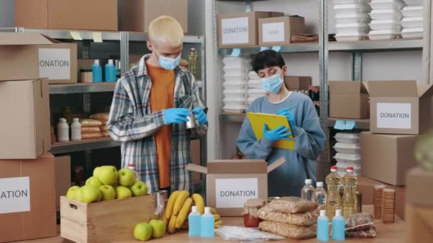 Man verpakking donatie doos terwijl vrouw met behulp van klembord — Stockvideo