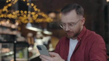 İş adamı kafede oturuyor, telefona bakıyor ve gülümsüyor, seviniyor..