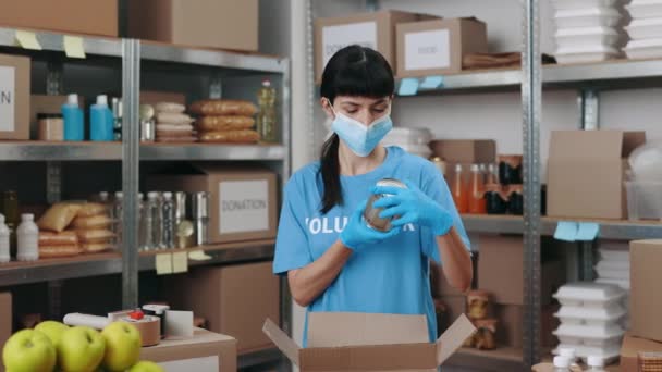 Mulher em máscara facial e caixas de arquivamento com alimentos não perecíveis — Vídeo de Stock