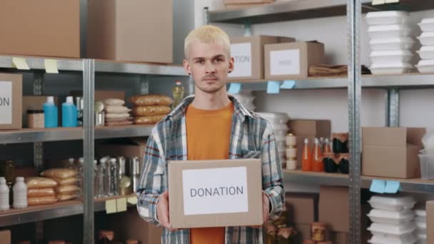 Caucásico hombre sosteniendo caja de donación entre banco de alimentos — Vídeo de stock