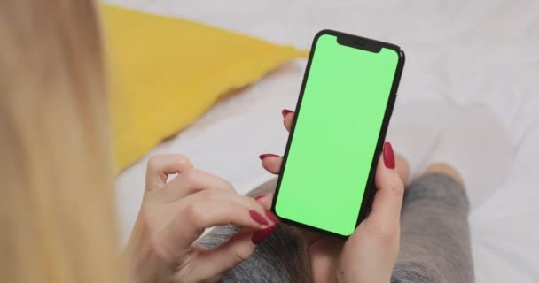 LVIV, UKRAINE - 5. März 2022: Frau liegt auf Bett und scrollt auf grünem leeren Bildschirm des modernen Smartphones. — Stockvideo