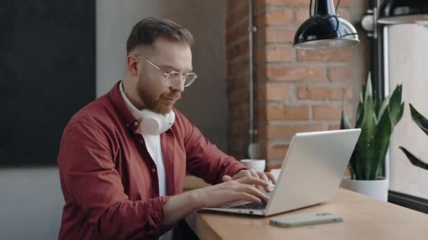 Freelancer kafede oturuyor ve bilgisayarına gülümseyerek bir şeyler yazıyor.. — Stok video