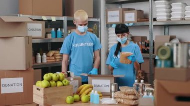 Yüz maskeli bir adam ve kadın bağış kutuları paketliyor.
