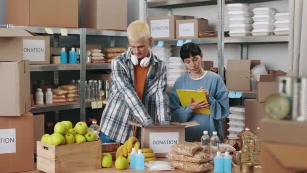 Mujer tomando notas mientras hombre embalaje cajas de donación — Vídeo de stock