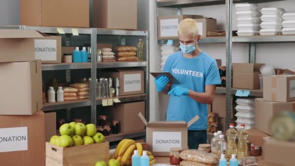 Máscara de homem no rosto usando comprimido para voluntariado no banco de alimentos — Vídeo de Stock
