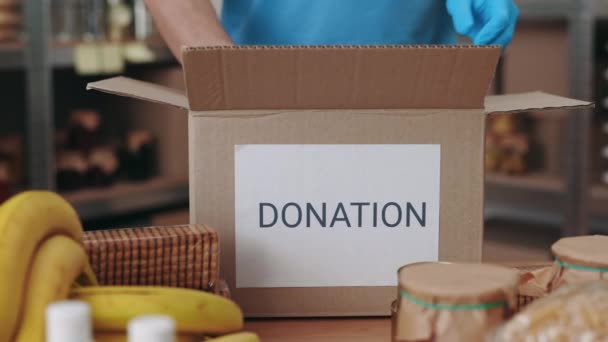 Detailní záběr dobrovolníka v rukavicích balení potravin v dárcovské krabici — Stock video