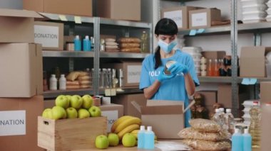 Yüz maskeli ve eldivenli kadın bağış kutusunu paketliyor.