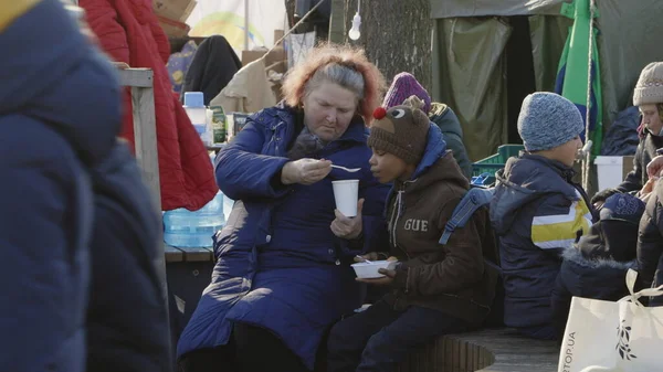 Lviv, Ukrayna - 15 Mart 2022: Lviv tren istasyonunda tren bekleyen mülteciler. Küçük çocuk evden ayrıldıktan sonra annesiyle oturup yemek yiyor..