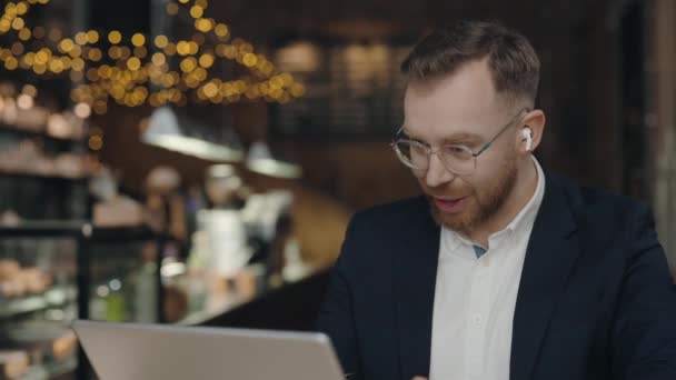 Αισιόδοξος επιχειρηματίας κάθεται στο καφέ και χρησιμοποιεί φορητό υπολογιστή. Αρσενική βιντεοκλήση. — Αρχείο Βίντεο