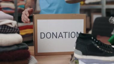 Erkek gönüllü ayakkabıları ayırıp depodaki dolaba koyuyor. İnsani yardım ve bağış konsepti. Kırpılmış görünüm.