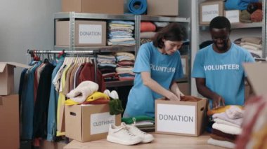 Esmer kadın ve çok ırklı adam depoda duruyor ve bağış için kıyafet düzenliyor. Arka plandaki raflara aitti. İnsani yardım kavramı.