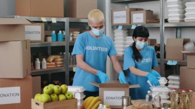 Yüz maskeli bir adam ve kadın bağış kutuları paketliyor.