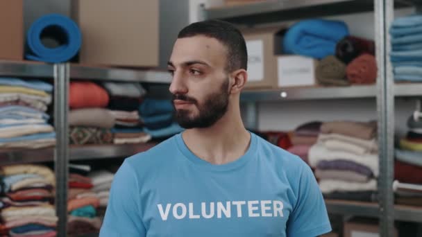 Portrait view of the caucasian volunteer man looking at the camera with smile. Shelves with belongings at the background. Humanitarian aid concept. — Stock Video